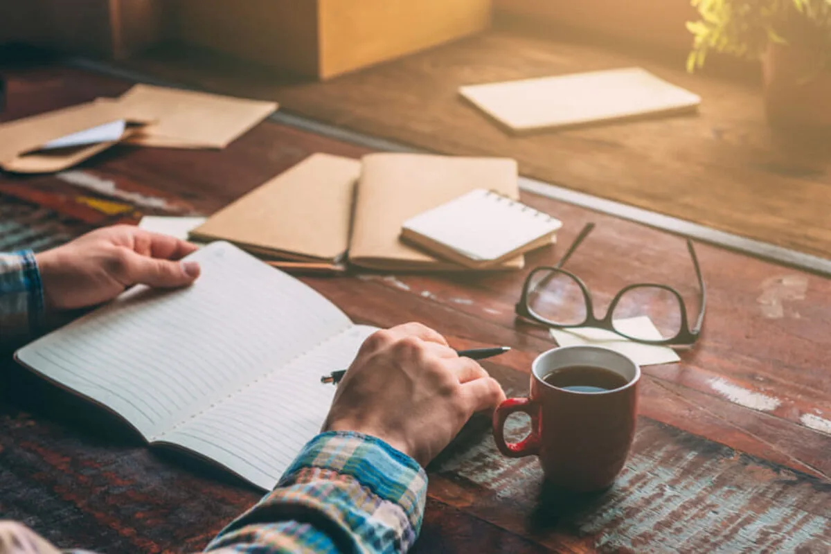Manos escribiendo en un cuaderno sobre una mesa de madera