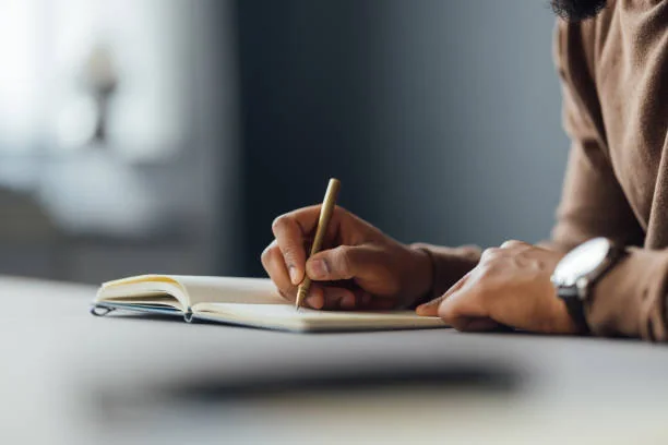 Mano escribiendo con una pluma dorada en un cuaderno